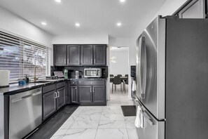A modern kitchen with dark cabinetry, stainless steel appliances, and a marble floor. - Modern Home By The Strip (Las Vegas)