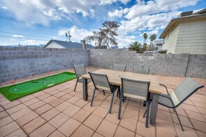 A patio with a table and chairs, a small putting green, and a brick wall. - Modern Home By The Strip (Las Vegas)