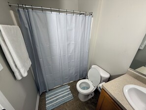Een badkamer met douchegordijn, toilet, wastafel en handdoekhouder.