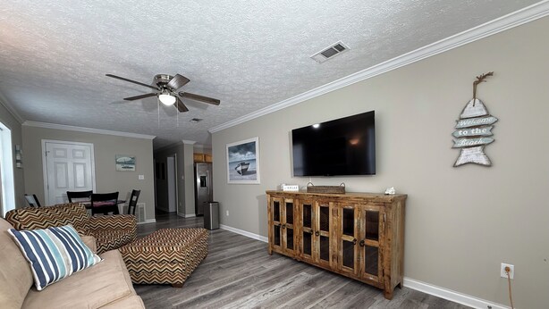 Ein Wohnzimmer mit beiger Couch, Holzschrank, Flachbildfernseher und Deckenventilator.