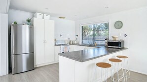 A modern kitchen with a stainless steel refrigerator, a microwave, and a large island with bar stools. - Stones Throw - Located right in the heart of Robe (Robe)