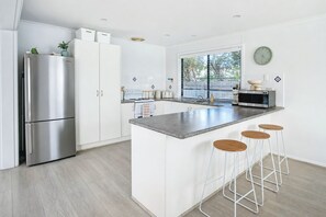 A modern kitchen with a stainless steel refrigerator, a microwave, and a large island with bar stools. - Stones Throw - Located right in the heart of Robe (Robe)