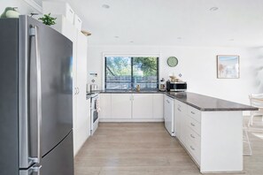 Eine moderne Küche mit einem Edelstahl-Kühlschrank, weißen Schränken, einem großen Fenster und Blick auf Grünflächen.