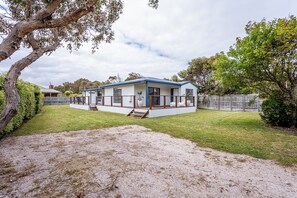 Einbungalow mit einer überdachten Veranda, einem umzäunten Garten und einer Auffahrt mit Kies.