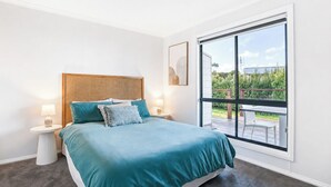 A bedroom with a large window, a bed with teal bedding, two bedside tables with lamps, and a rattan headboard. - Stones Throw - Located right in the heart of Robe (Robe)