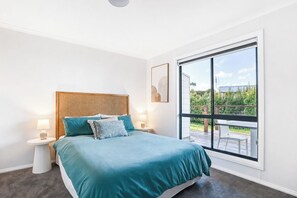 A bedroom with a large window, a bed with teal bedding, two bedside tables with lamps, and a rattan headboard. - Stones Throw - Located right in the heart of Robe (Robe)