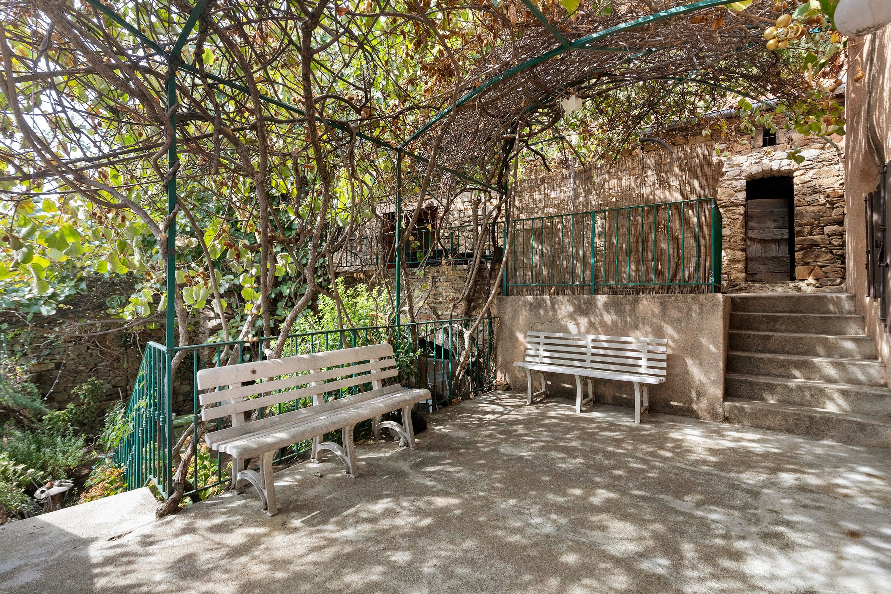 A stone staircase leading to a building, a white bench, and a green metal railing.