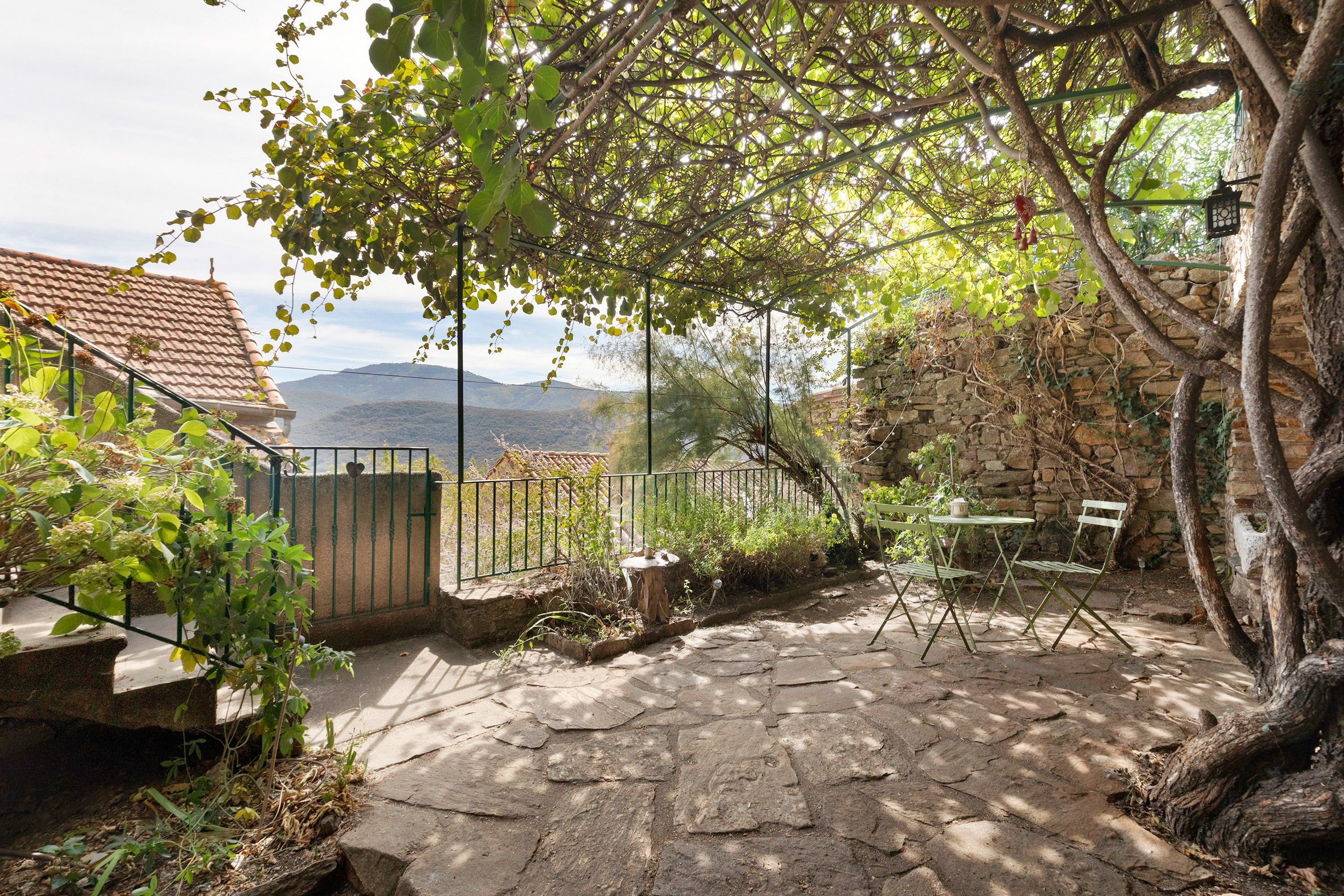 Une terrasse en pierre offrant une vue sur les montagnes, un mur en pierre et un portail en métal.