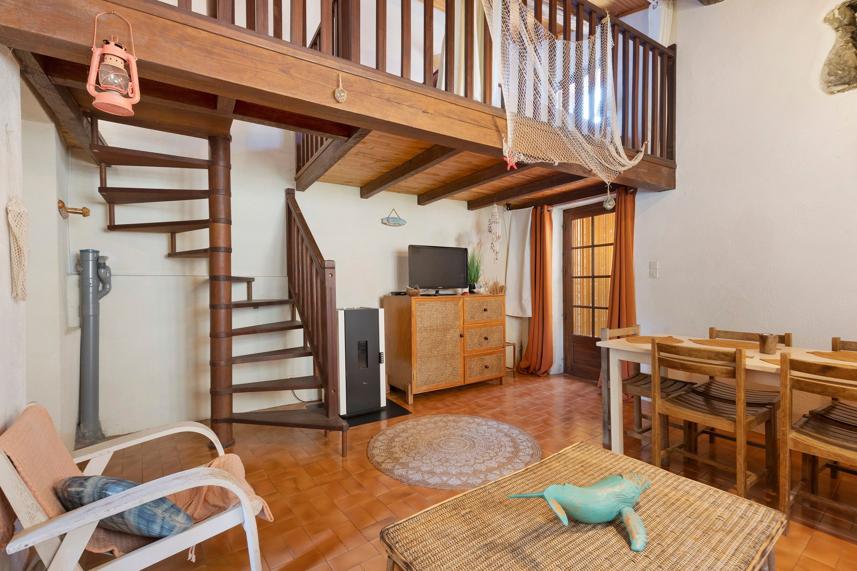 Ampla sala de estar com escada de madeira, televisão e mesa de jantar com cadeiras.