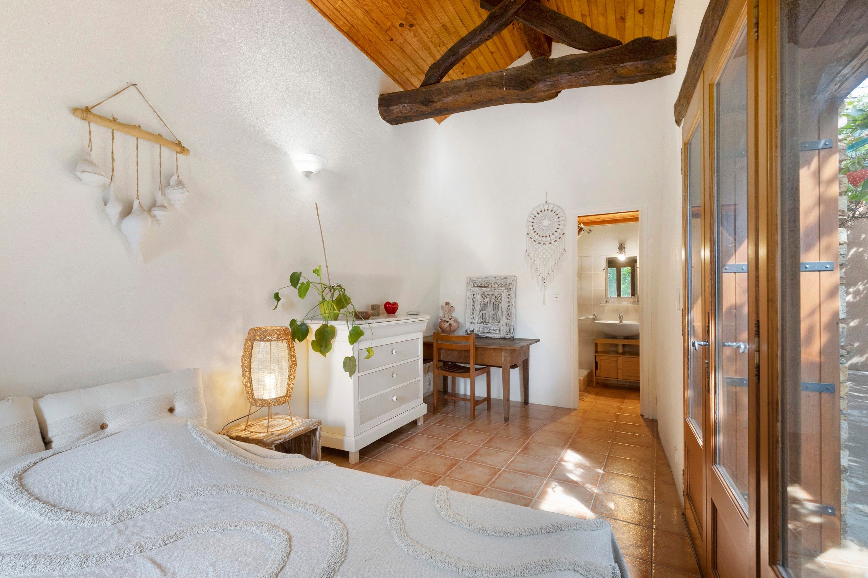 Quarto com cama, cômoda, escrivaninha e cadeira. Há uma janela com vista para o exterior.