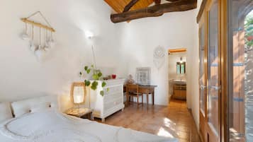 Quarto com cama, cômoda, escrivaninha e cadeira. Há uma janela com vista para o exterior.