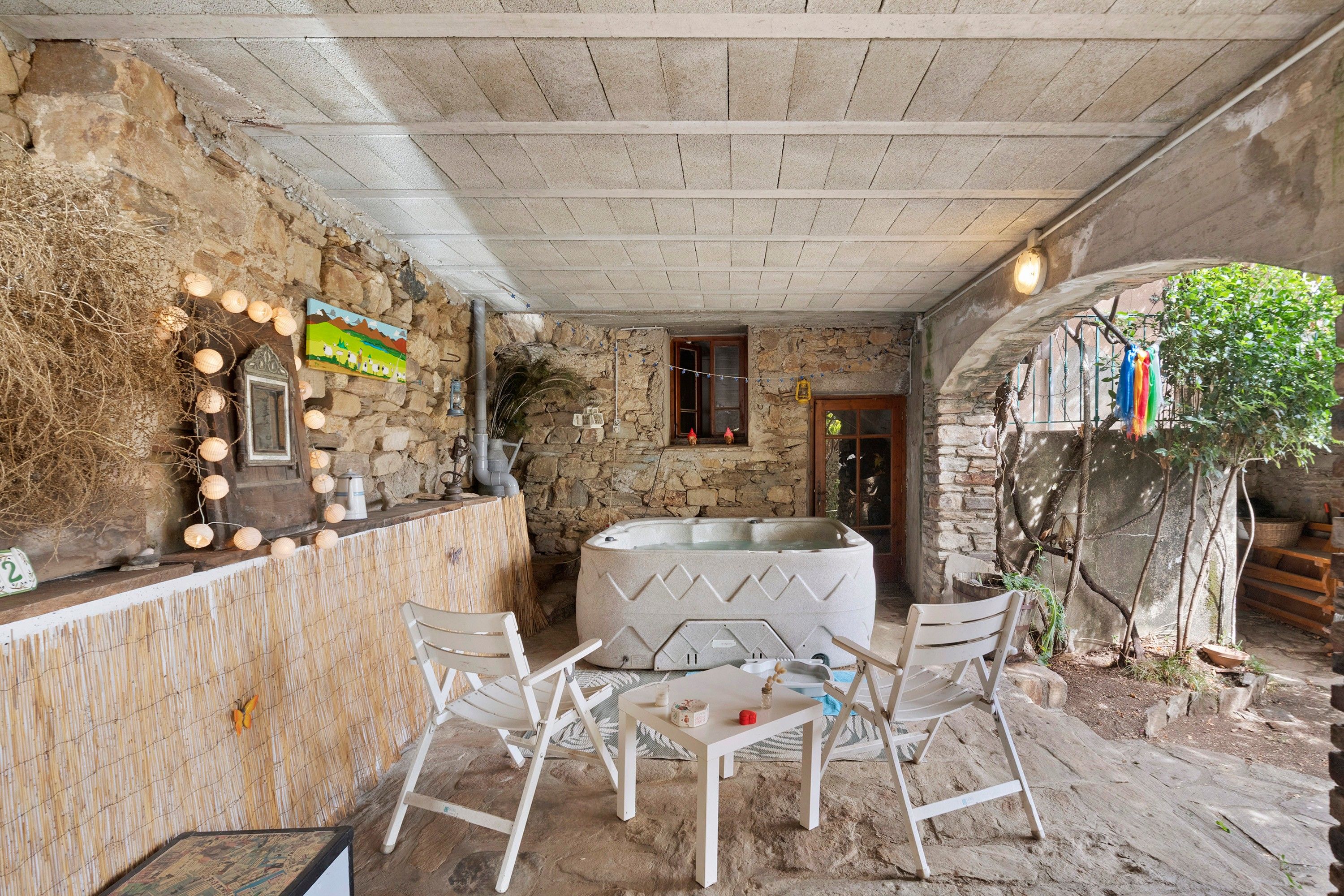 Un espacio de descanso al aire libre de estilo rústico con paredes de piedra, una bañera de hidromasaje y una mesa de madera con sillas.