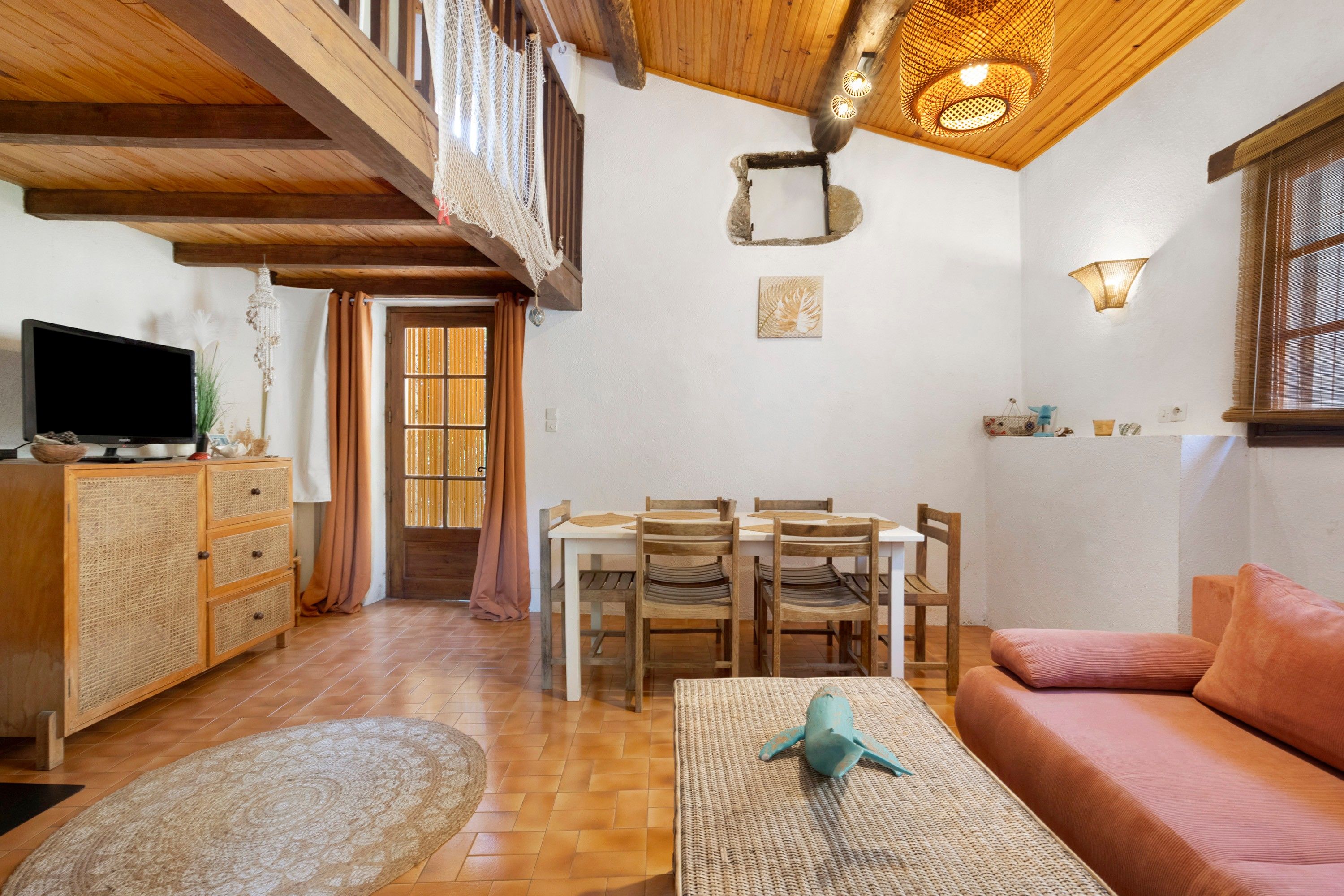 A cozy living room with a television, wooden furniture, a sofa, and a dining area with chairs.