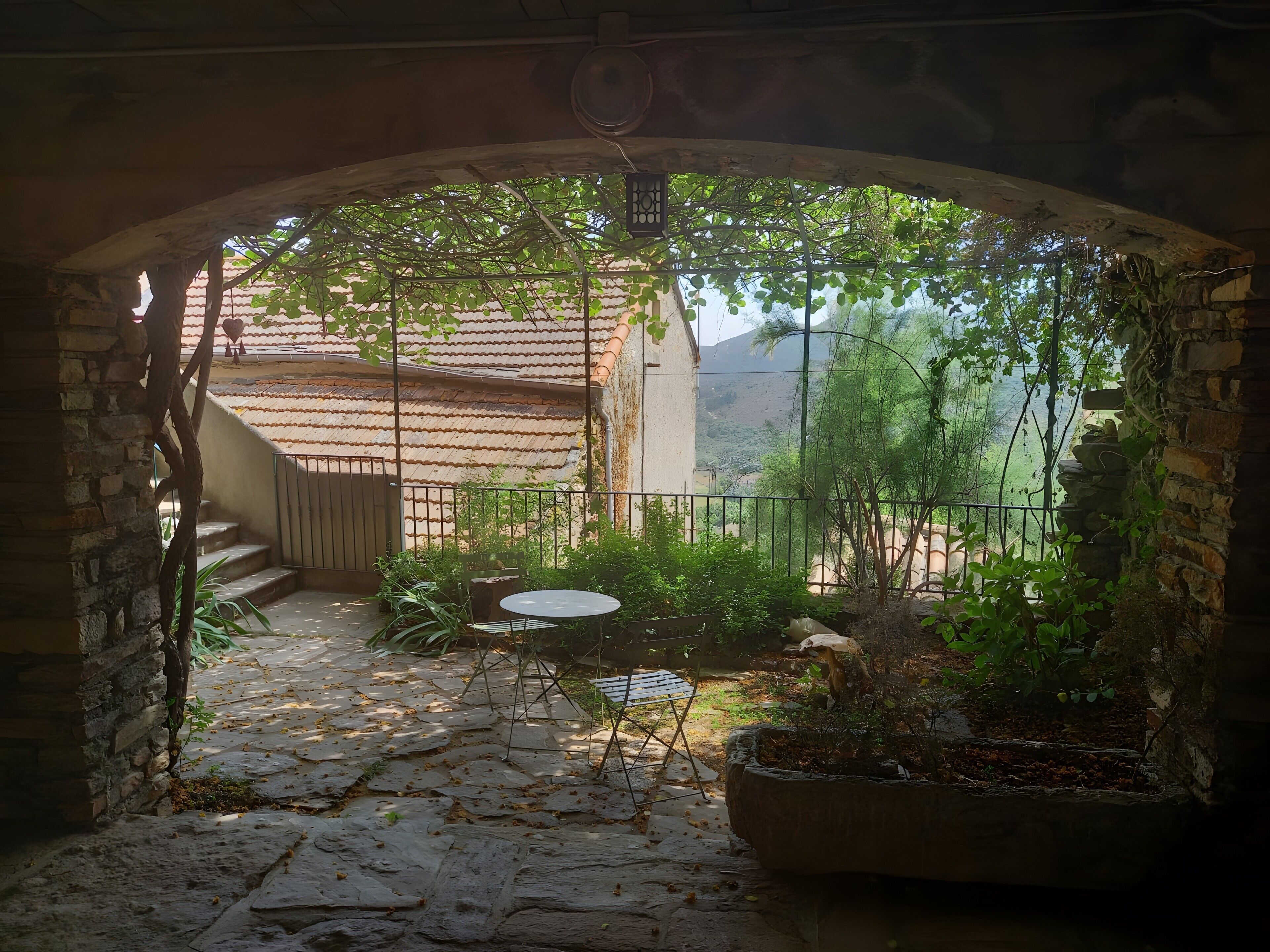 Un portail en arc donnant sur un patio doté d’un sol en pierre, d’une table et de chaises.