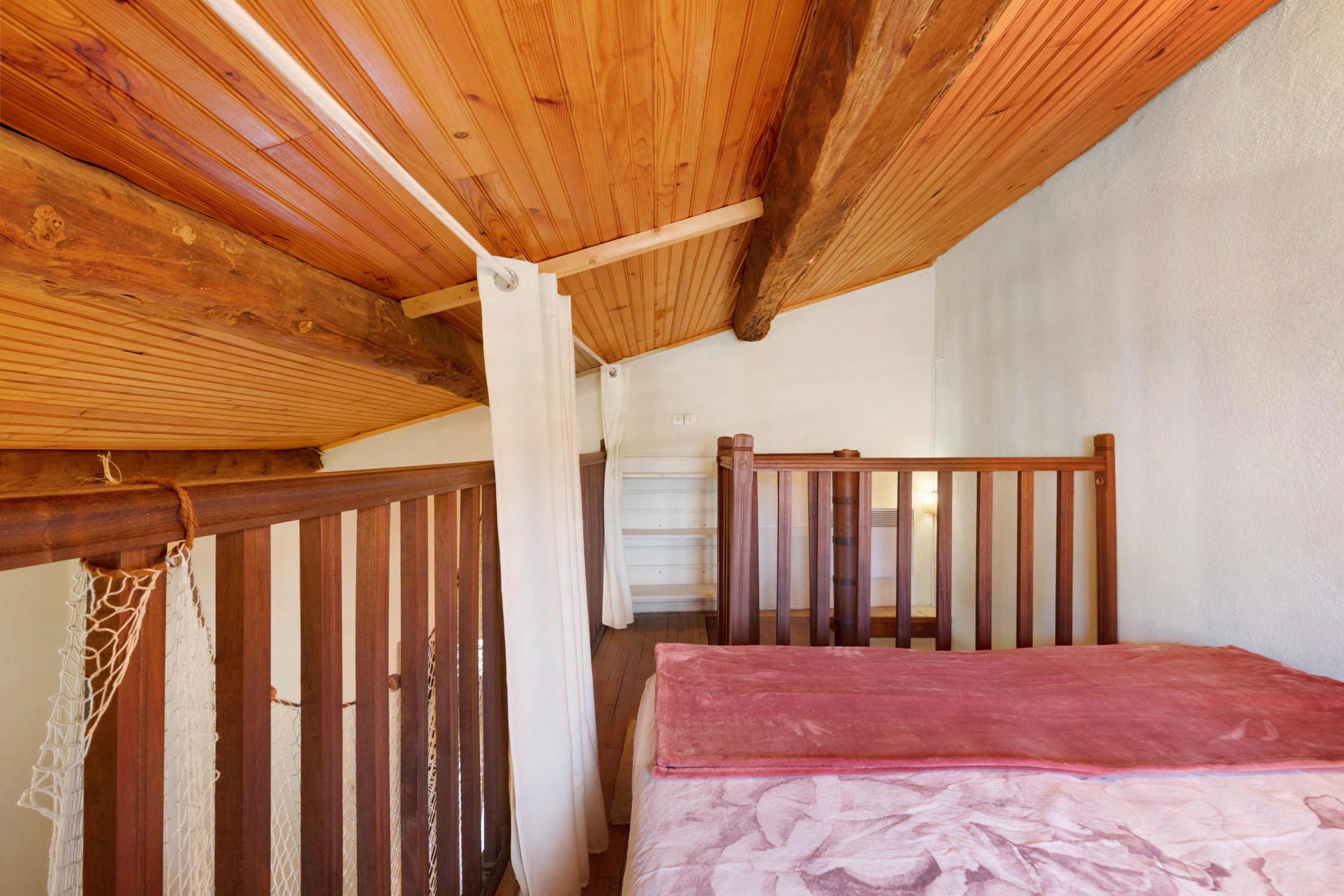 A wooden room with a sloped ceiling, a bed with a red blanket, and a wooden railing.