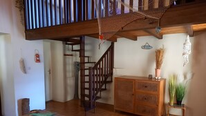 Un escalier en bois avec une rampe, une table en osier avec un coussin et un meuble orné de plantes décoratives.