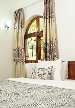 Een slaapkamer met een bed, een raam met gordijnen en een wandlamp.
