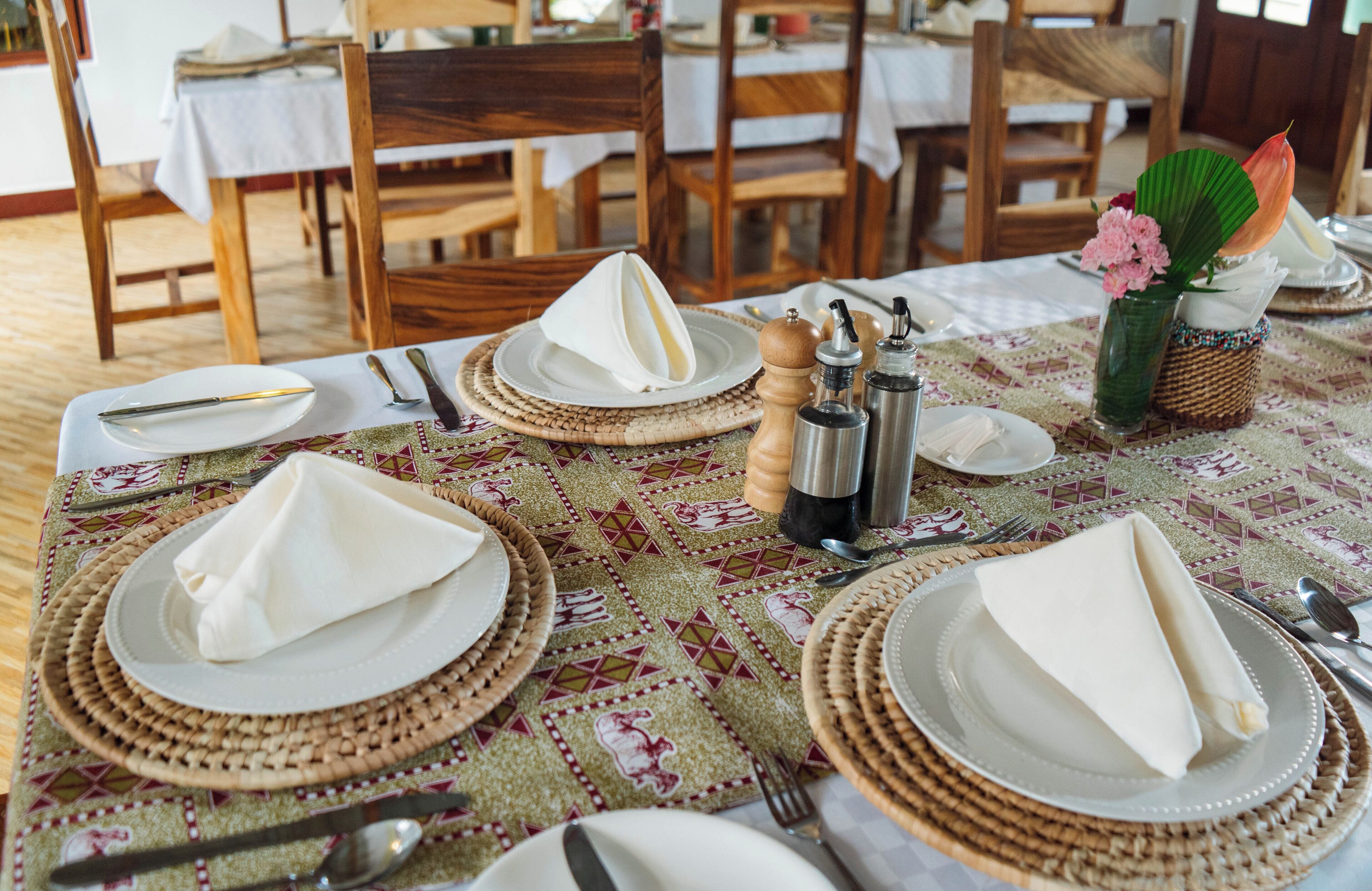 A dining table set with white plates, cutlery, and napkins, with a patterned tablecloth and a vase with flowers.