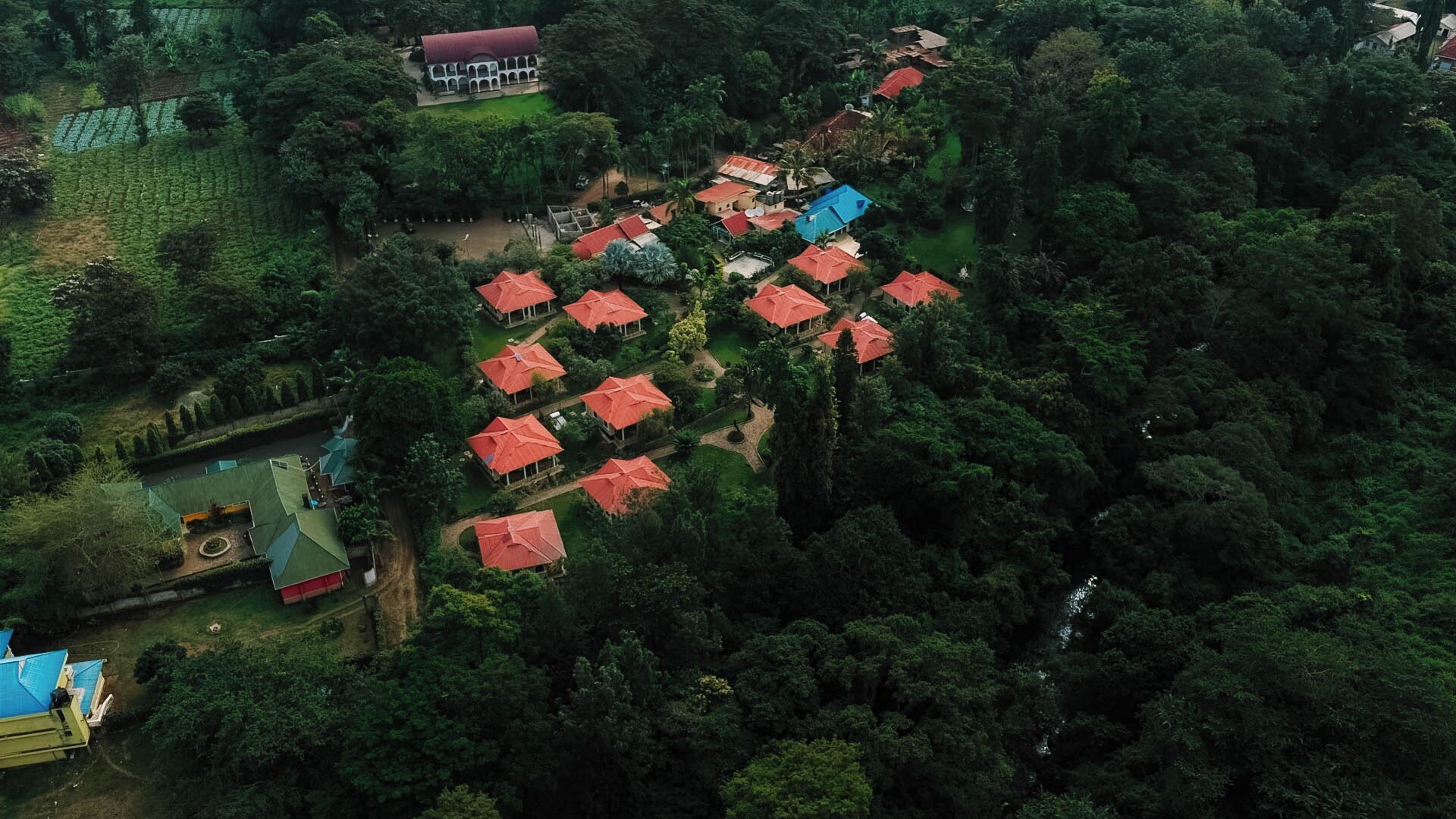 An aerial view of a resort with multiple red-roofed structures, surrounded by dense greenery and a few buildings with blue roofs.
