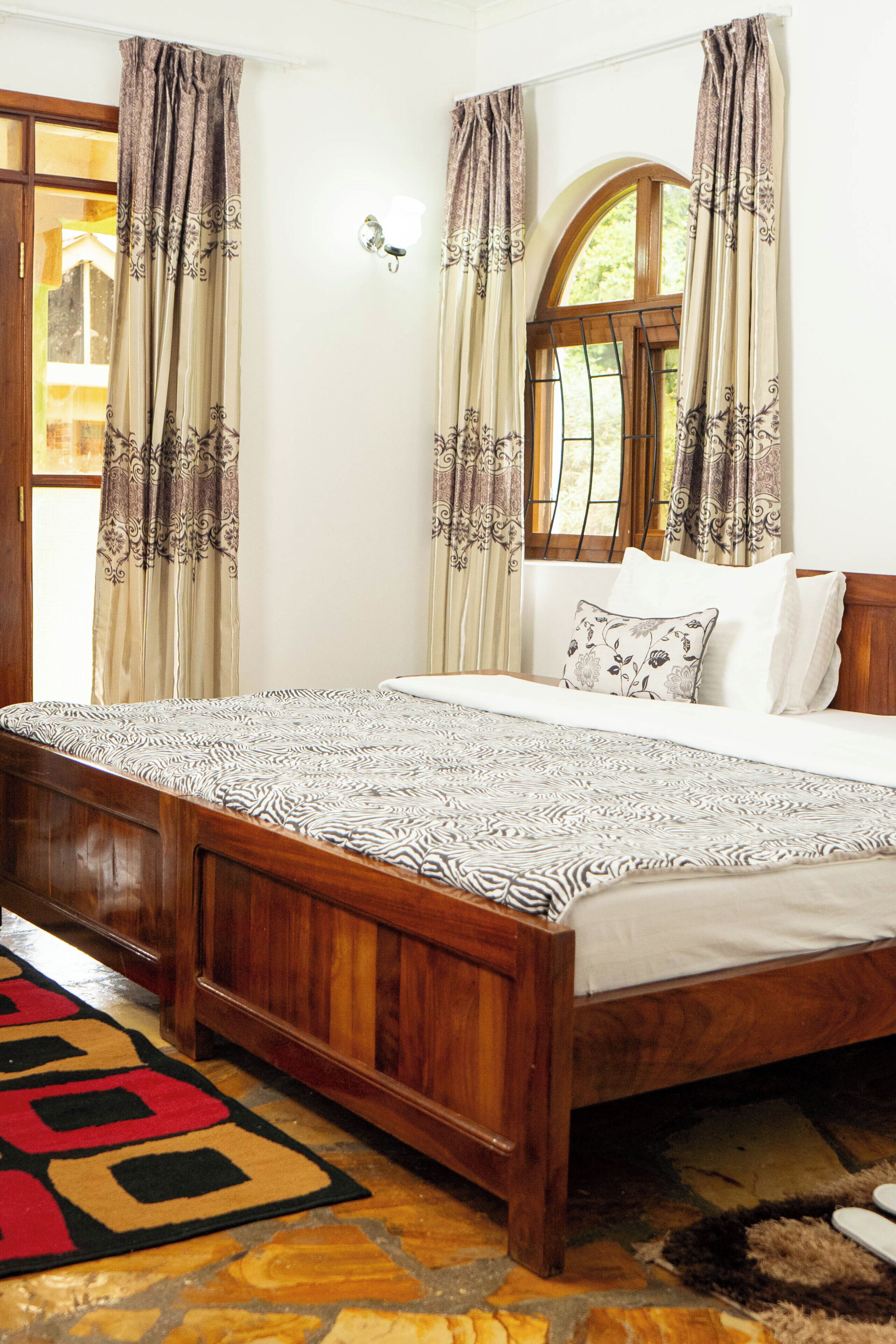 A bedroom with a wooden bed, patterned bedspread, and curtains with floral designs.