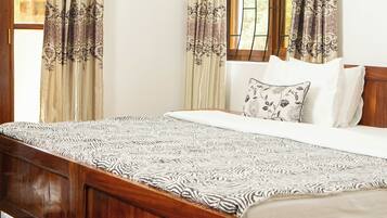 A bedroom with a wooden bed, patterned bedspread, and curtains with floral designs.