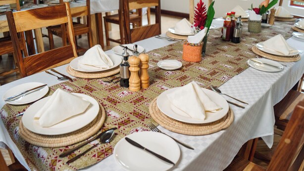 A dining table set with plates, cutlery, and napkins, with a patterned table runner and wooden chairs.