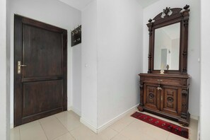 A closed dark wooden door with a metal handle, a white wall, and a wooden cabinet with a mirror and decorative items. - Apartment with Soul | Bedroom (Kraków)