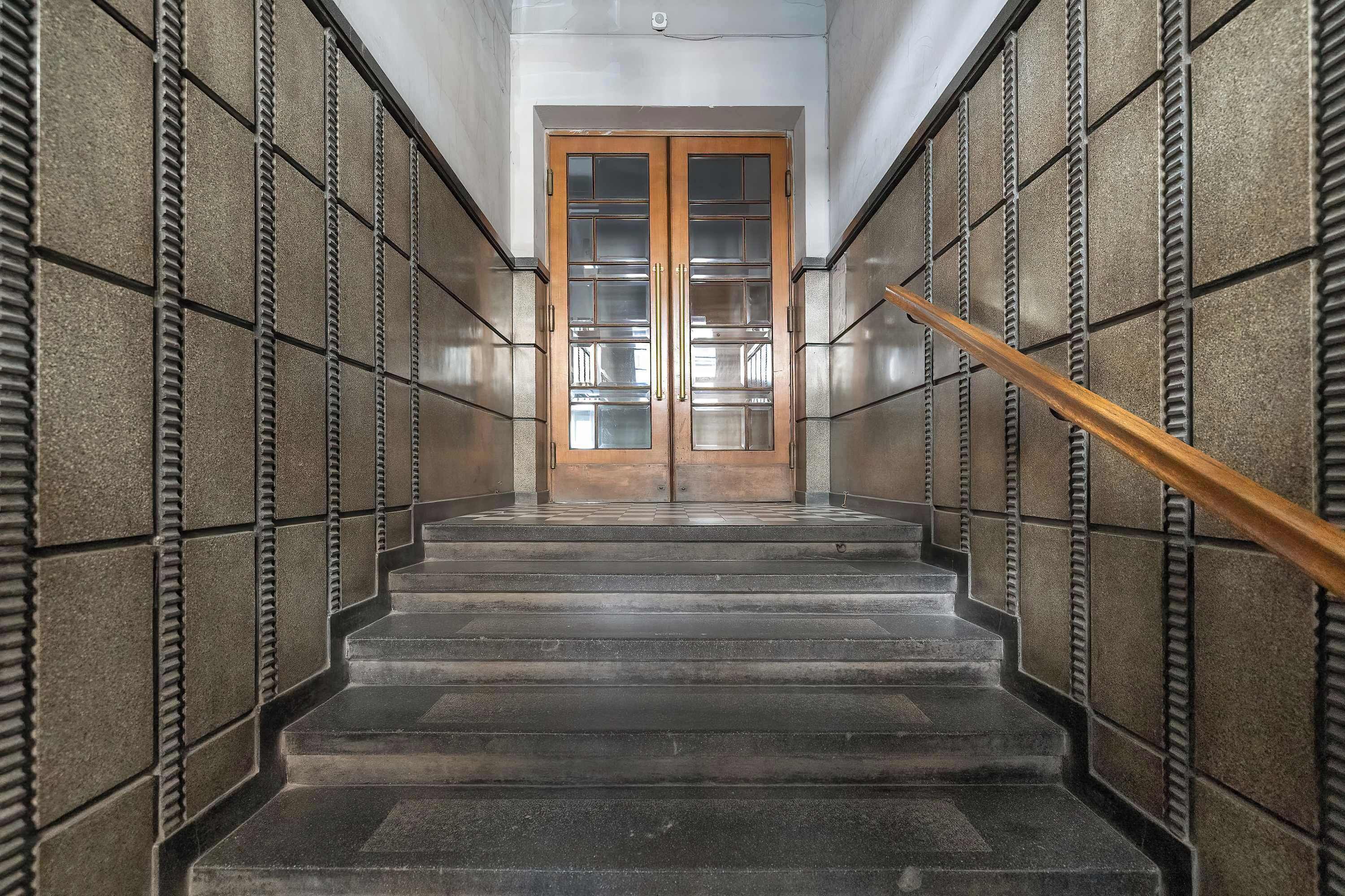 A staircase with a wooden handrail leading to a door with glass panels.