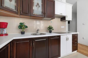 A kitchen with dark brown cabinets, a white countertop, a red Bosch coffee maker, and two potted plants. - Apartment with Soul | Bedroom (Kraków)