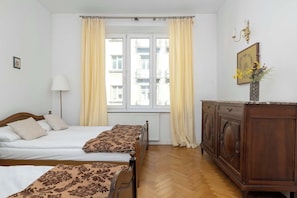 A hotel room with two beds, a wooden dresser, a radiator, and a window with curtains. - Apartment with Soul | Bedroom (Kraków)