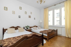 Ein Hotelzimmer mit zwei Holzbett, einem Nachttisch mit Lampe, einem Fenster mit Vorhängen und Wandbildern.