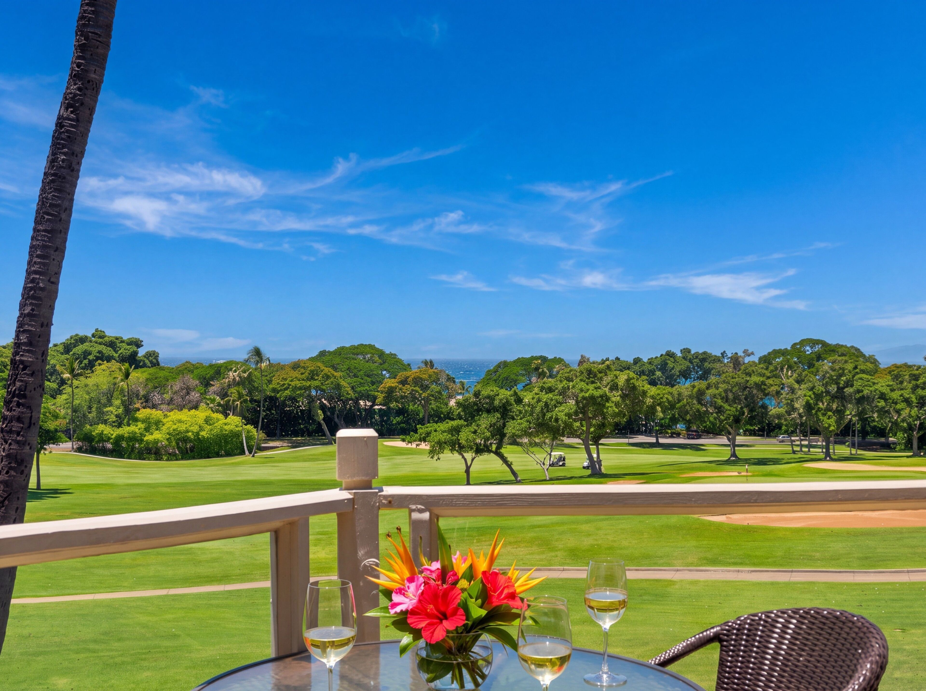 Ein Tisch mit zwei Weingläsern und einer Blumenvase, mit Blick auf einen Golfplatz bei blauem Himmel.