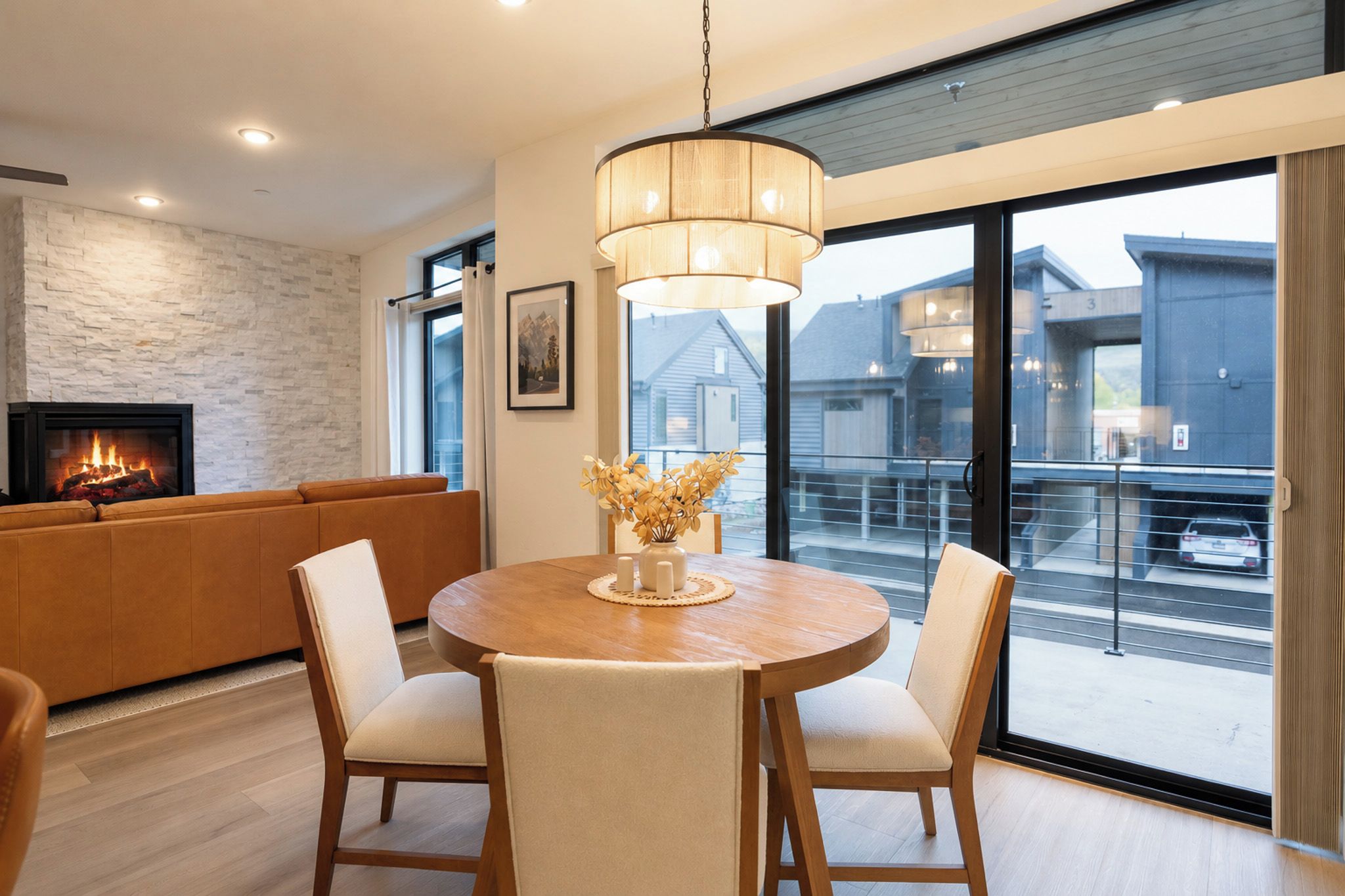 Un salon moderne avec une cheminée, une table à manger ronde entourée de chaises et une grande fenêtre donnant sur des immeubles.
