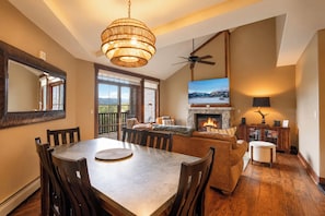 A spacious living area with a fireplace, a dining table, and a large window offering a view of the outdoors. - Crystal Peak Highpoint Condo: Ski In/Out, Mountain Views (Breckenridge)
