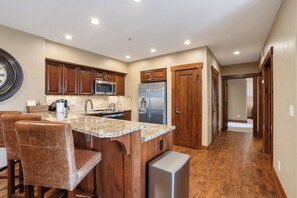 A kitchen with wooden cabinets, a stainless steel refrigerator, and a granite countertop. - Crystal Peak Highpoint Condo: Ski In/Out, Mountain Views (Breckenridge)