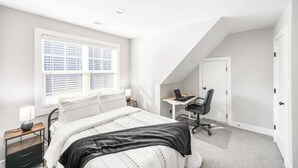 Quarto com cama, escrivaninha, cadeira, janela com persianas e porta.