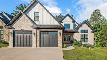 Une maison à deux étages avec une façade en pierre, un garage à deux portes et une pelouse bien entretenue.