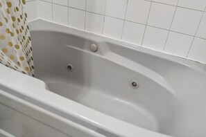 A bathtub with two faucets and a drain, set against a tiled wall.
