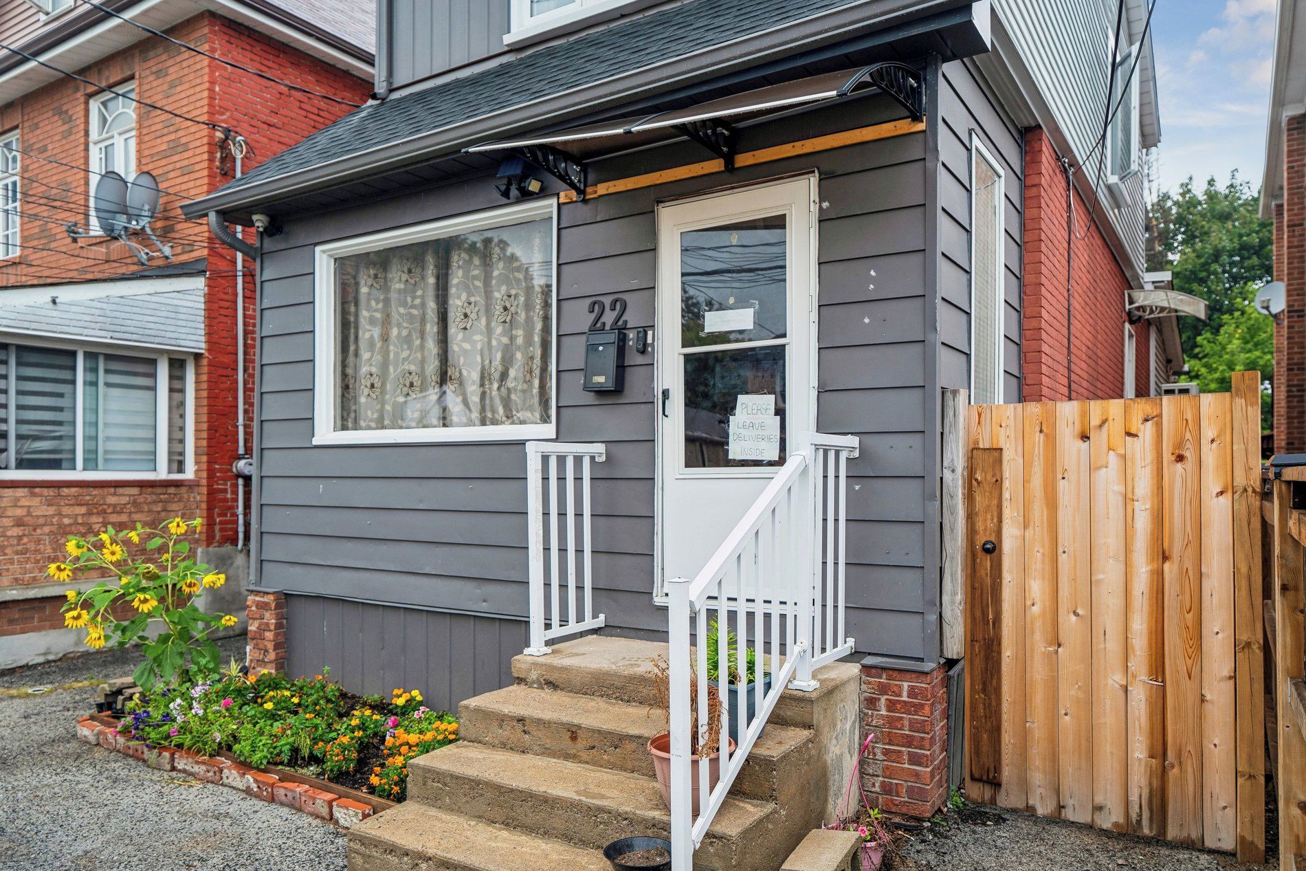 A residential house with a grey exterior, a white front door, and a wooden gate.