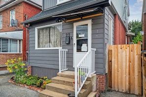 A residential house with a grey exterior, a white front door, and a wooden gate.