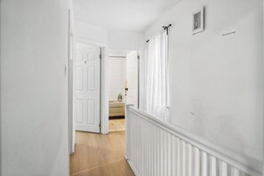 A hallway with white walls, a wooden floor, and a white door leading to another room.