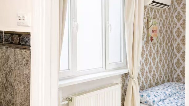 Ein Schlafzimmer mit Fenster, Klimaanlage, Heizkörper und strukturierter Wandgestaltung.