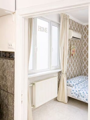 A bedroom with a window, an air conditioning unit, a radiator, and patterned wallpaper. - Quinet Downtown (București)