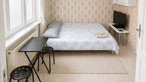 Ein kleines Schlafzimmer mit einem Bett, einem Fernseher, einem Schreibtisch und einem Stuhl.