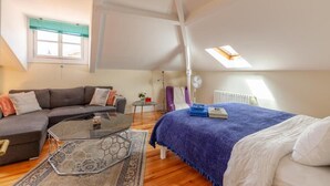 A modern loft bedroom with a glass coffee table, a sofa, a bed with a blue blanket, and a skylight. - S.K.Y. Accommodations Family studios  (Coimbra)