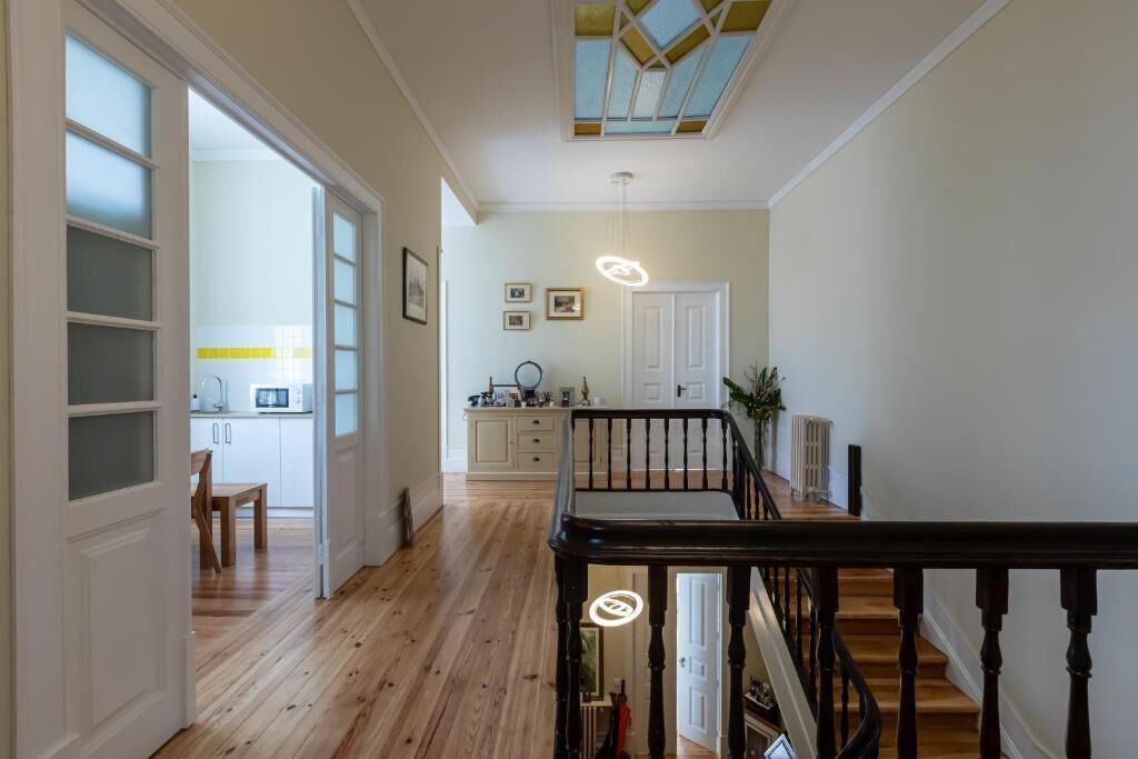 A hallway with wooden flooring, a staircase with black balusters, and a kitchen area in the background.