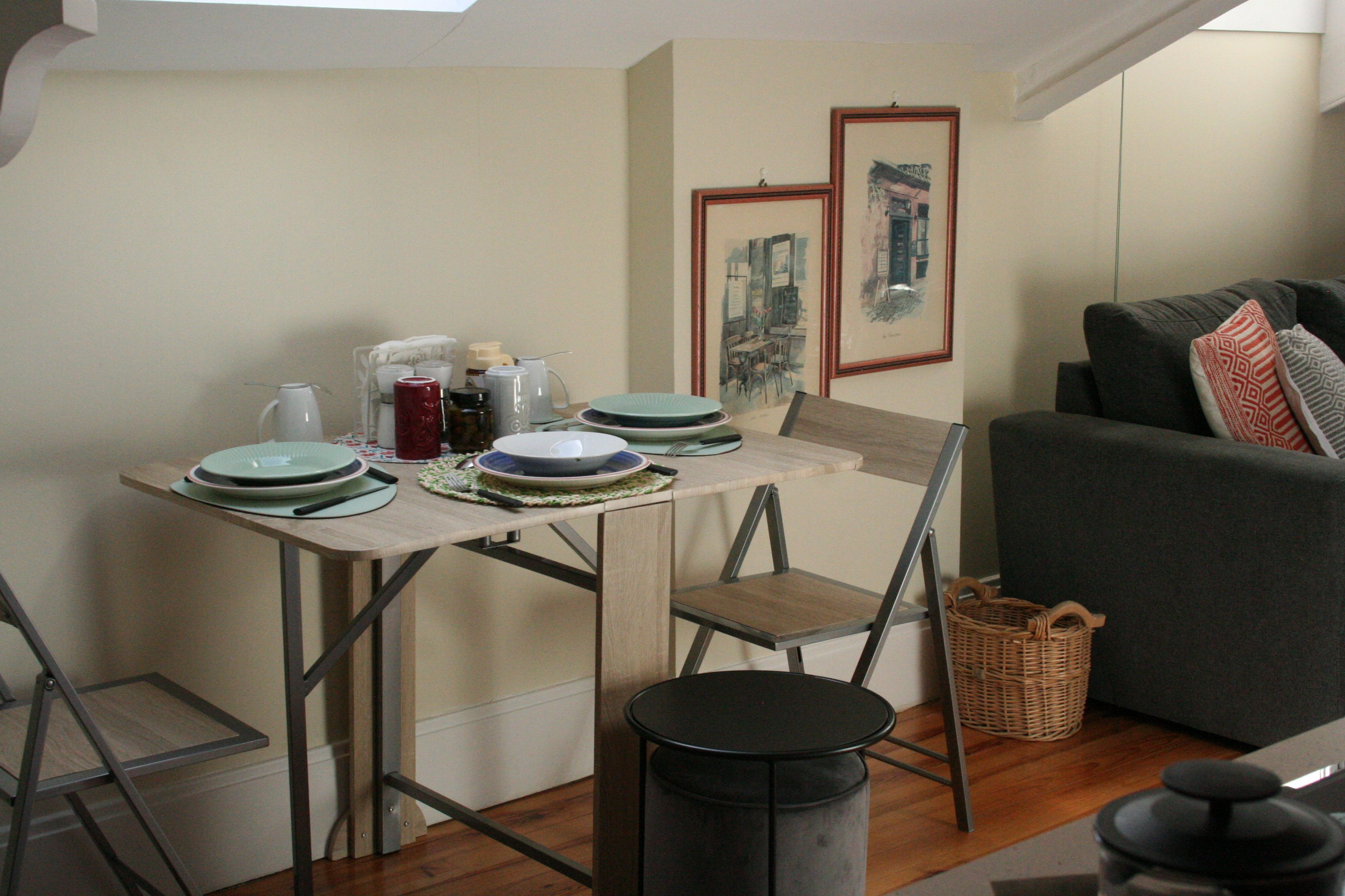 Un espace de vie compact comprenant une table à manger, des chaises, une petite table ronde, un canapé et un panier.