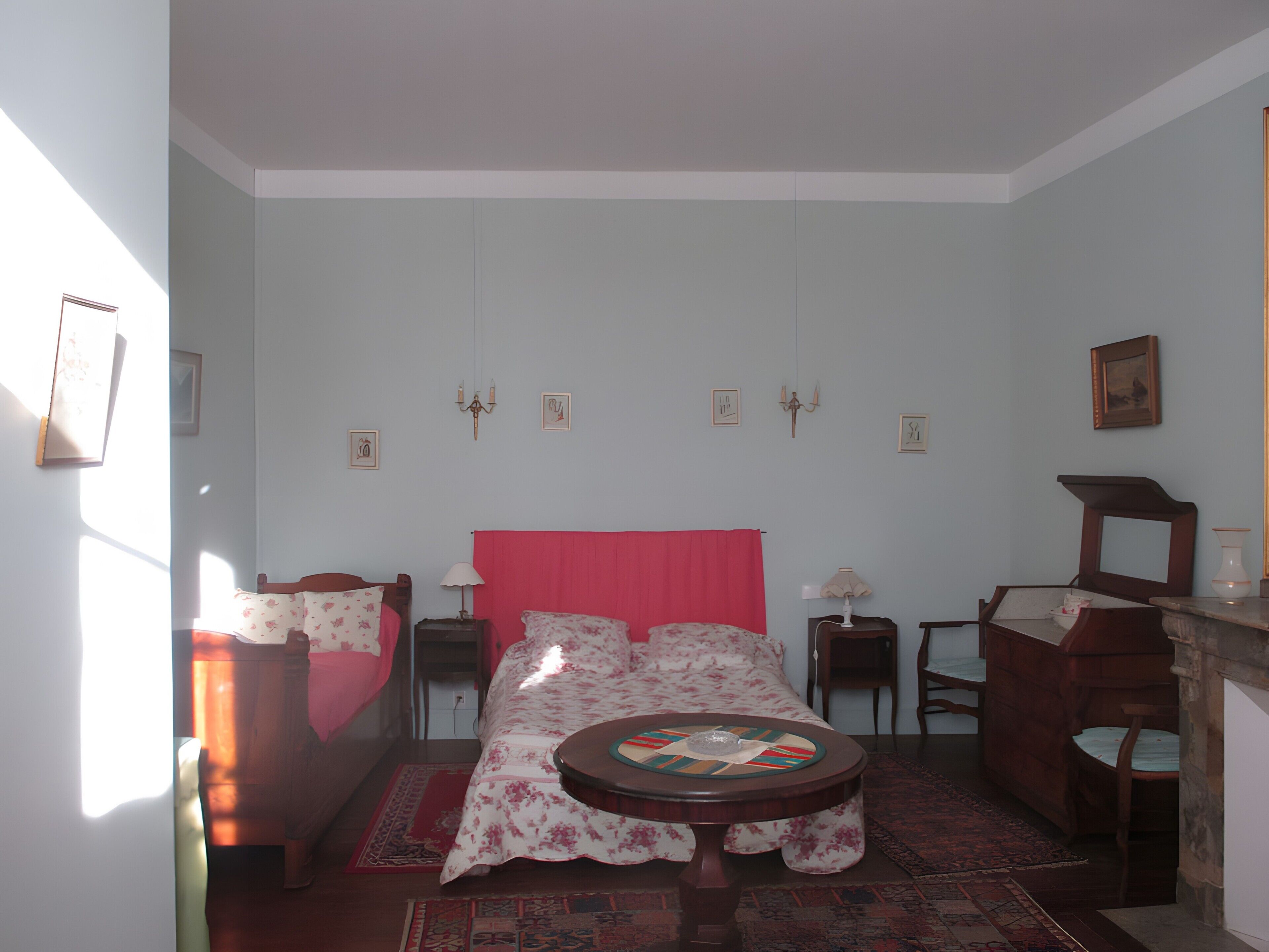 Een slaapkamer met een bed, een ronde tafel, een stoel, een dressoir en een spiegel.