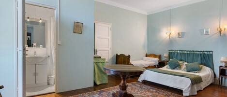 A bedroom with a bed, a round table, a mirror, a bathroom with a sink, and a door.