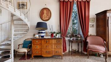 Une pièce avec une commode en bois, une chaise, une table avec une lampe, un rideau rouge et un escalier.